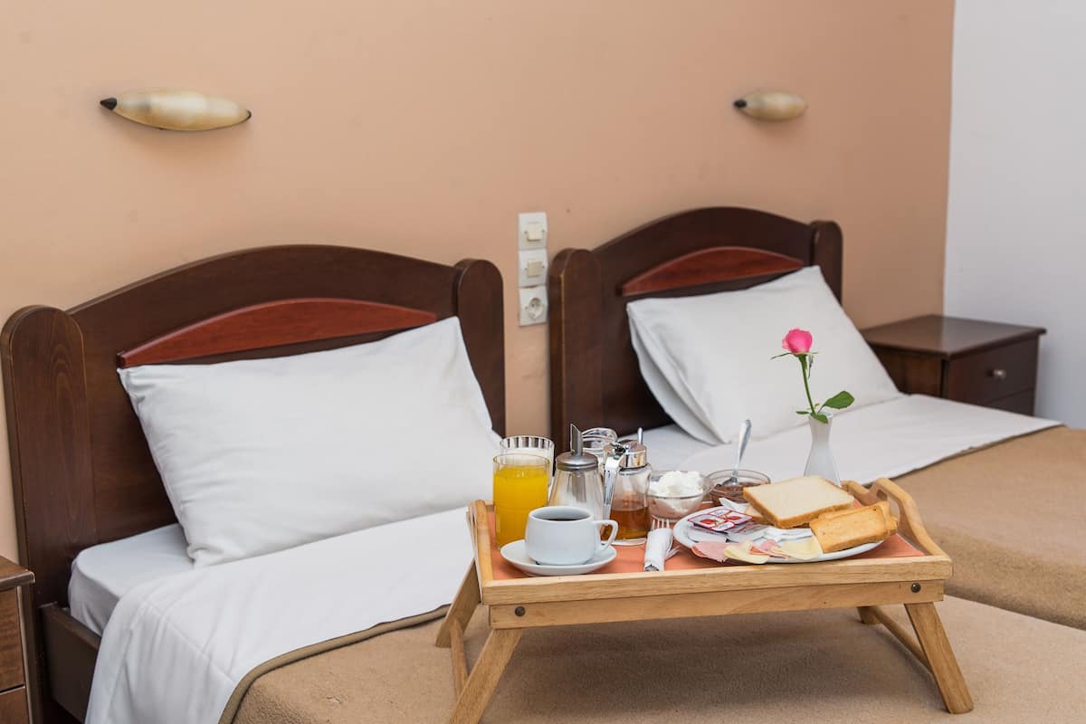 A hotel room with two wooden beds, white bedding, a tray with breakfast items, and a vase with a single pink flower.
