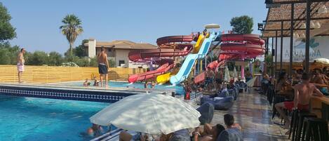 A pool area with multiple water slides and a bar area with umbrellas.