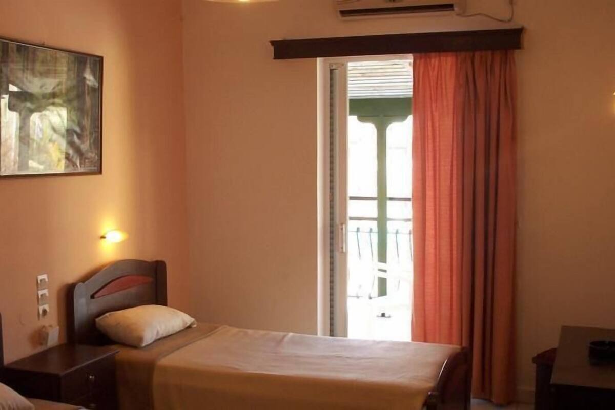 A hotel room with a bed, a nightstand, a lamp, a painting on the wall, and a window with curtains.
