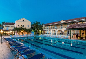 A swimming pool with lounge chairs, a bar area, and buildings with balconies. - Perkes Hotel (Zakynthos)