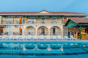 A hotel with a swimming pool, outdoor seating, and a covered area. - Perkes Hotel (Zakynthos)