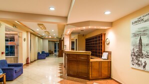 A hotel lobby with a reception desk, blue seating area, and a wall-mounted clock.