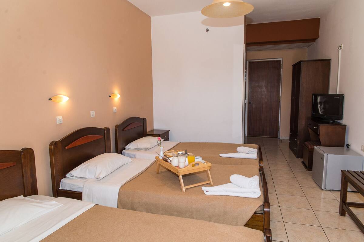A hotel room with two beds, a wooden bedside table with a tray of breakfast items, a television, and a small refrigerator.