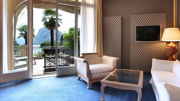 A room with a large sliding glass door leading to a balcony with outdoor furniture and a view of mountains.