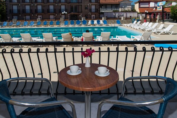 Un área junto a la piscina con sillones de descanso y una mesa con tazas y un florero.
