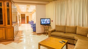 A hotel living room with a sofa, a coffee table, a TV, and a wooden cabinet.