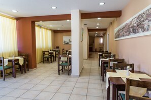 A dining area with multiple tables and chairs, a tiled floor, and a corridor leading to another section. - Perkes Hotel (Zakynthos)