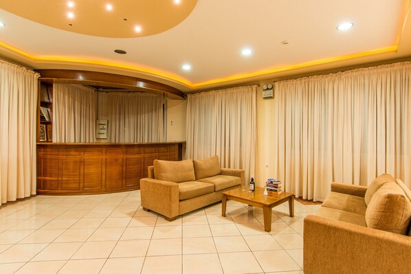 A living room with a sofa, armchair, and coffee table. There is a wooden cabinet and a curtain-covered window.