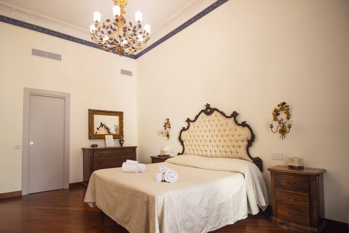 A bedroom with a large bed, a dresser, a nightstand, a chandelier, and a mirror.