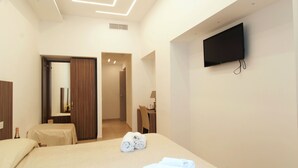 Una habitación de hotel con una cama, un televisor montado en la pared, un escritorio con una silla y una puerta que da a otra habitación.