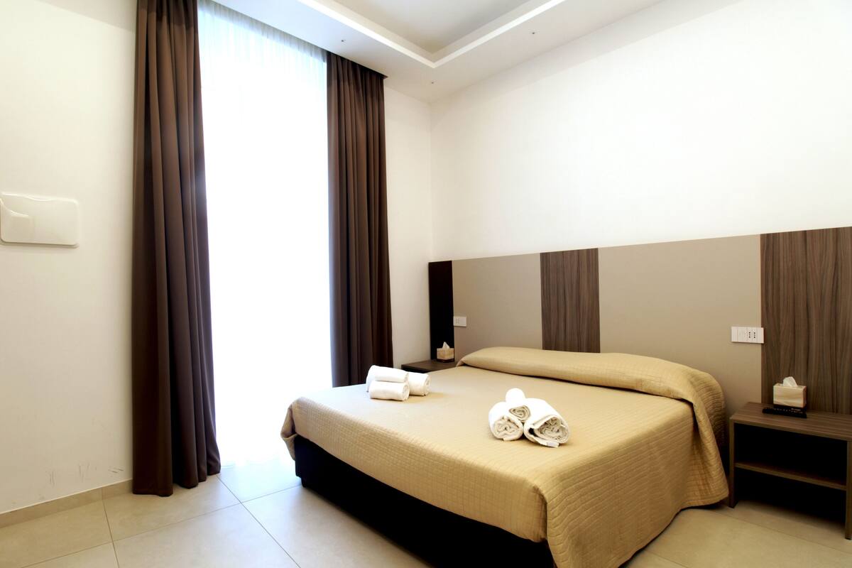 A hotel room with a large bed, a nightstand, and a bedside table.