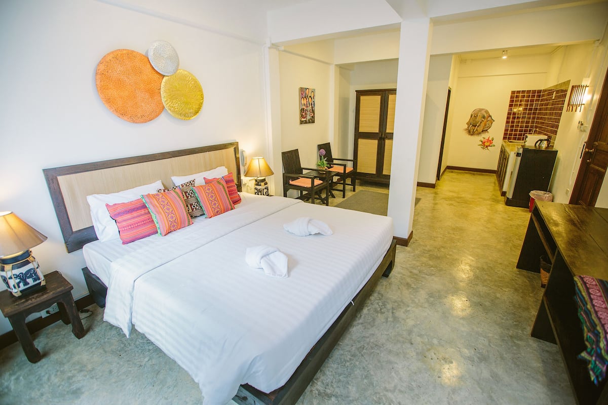 Habitación de hotel con una cama grande, una mesita de noche con lámpara, una silla y una pequeña mesa con un florero.