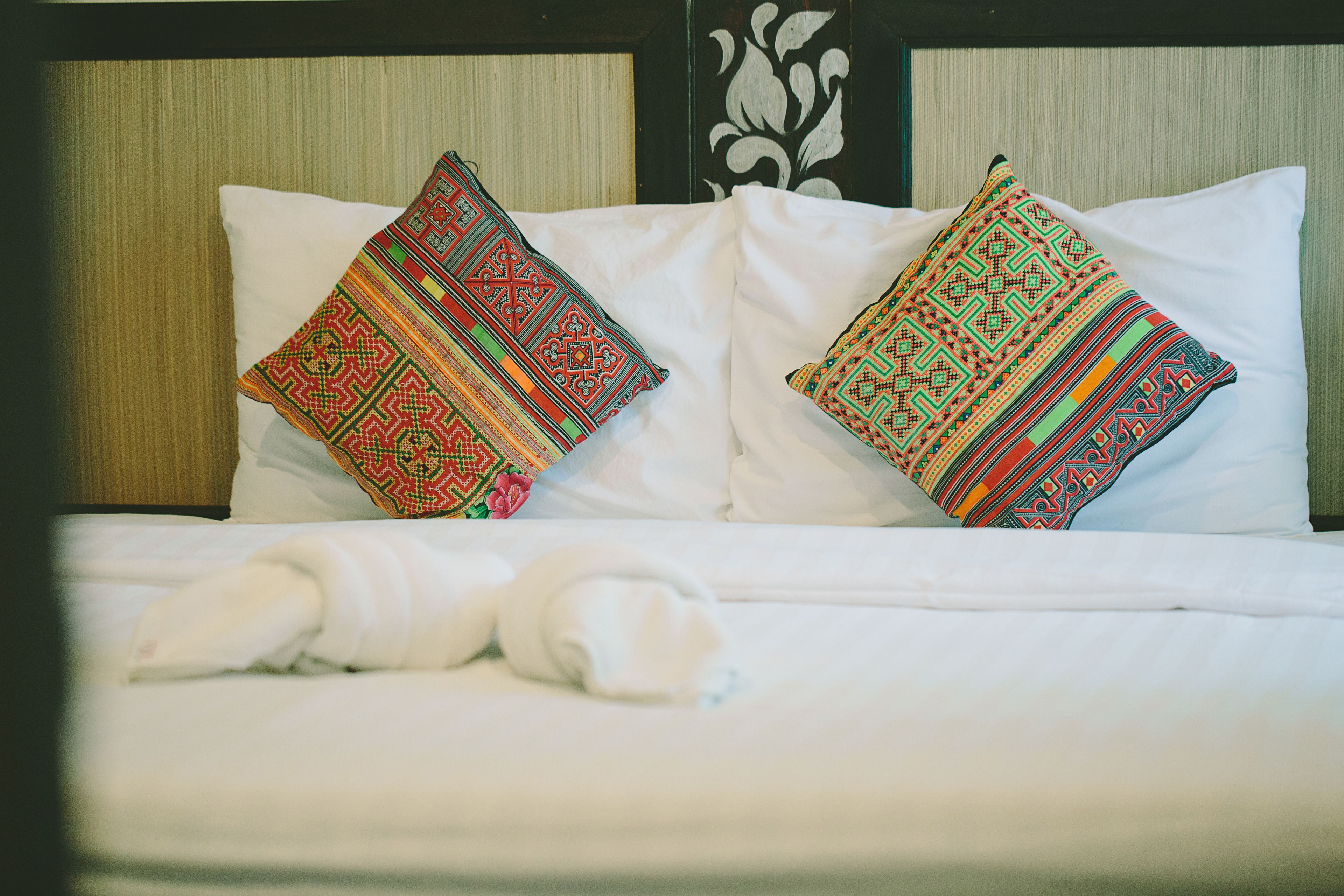 Una cama con sábanas blancas y dos almohadones decorativos con diseños elaborados.