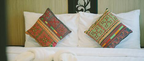 Una cama con sábanas blancas y dos almohadones decorativos con diseños elaborados.