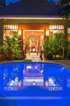 A poolside area with a clear view of the pool, potted plants, and a well-lit entrance to a building. - The Odyssey Serviced Apartment (Chiang Mai)