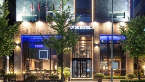 Een hotel met een moderne gevel, diverse vlaggen en een 'Grand Open' bord.