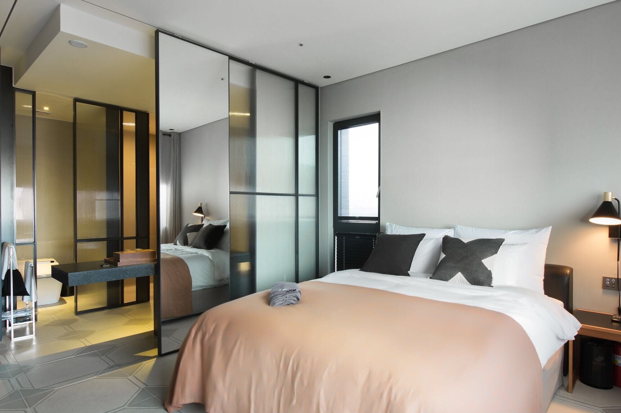Ein modernes Hotelzimmer mit einem großen Bett, einem Spiegel, einem Schreibtisch und Blick auf die Stadt.