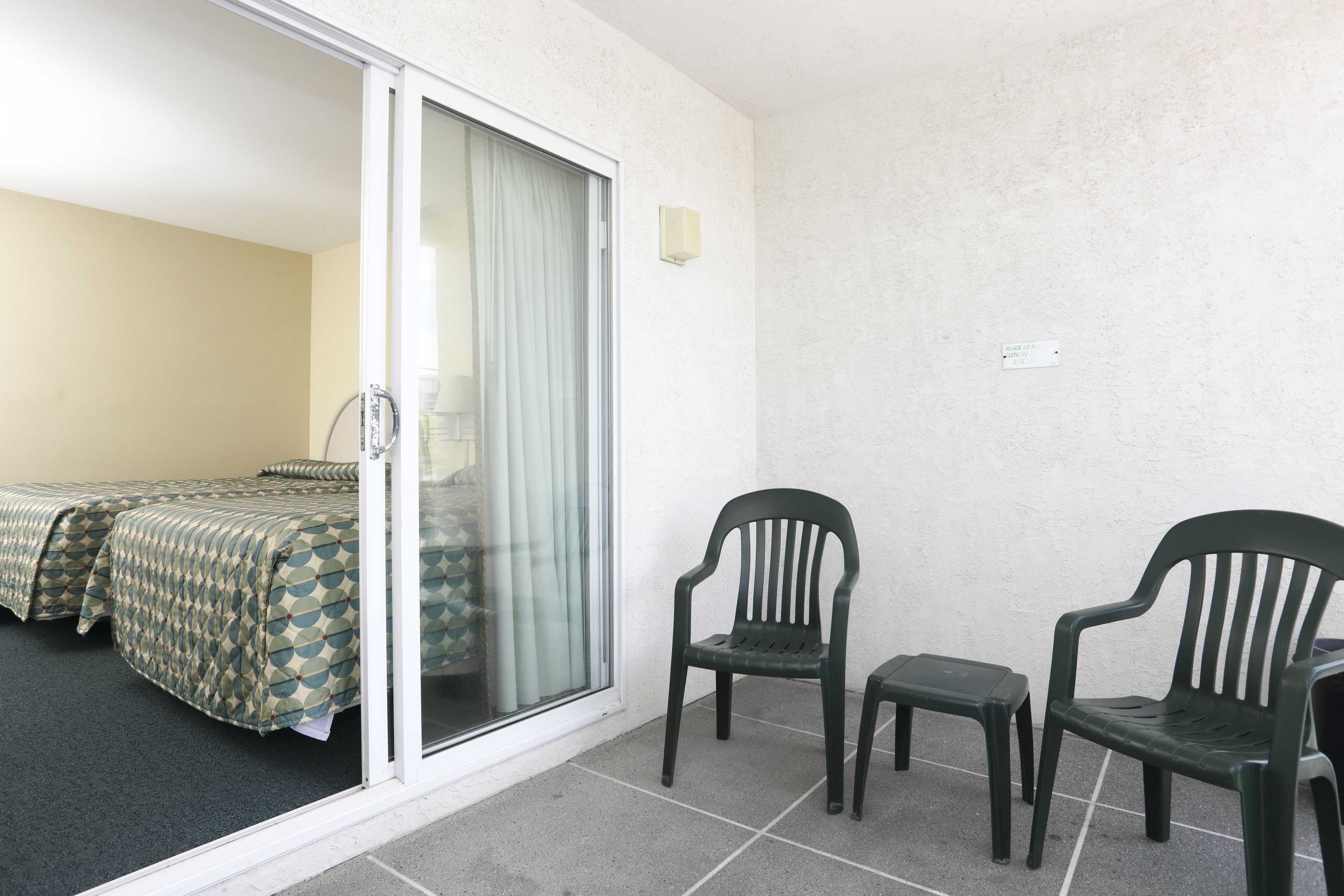 A room with two beds, a sliding glass door, and two chairs.