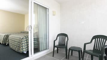 A room with two beds, a sliding glass door, and two chairs.