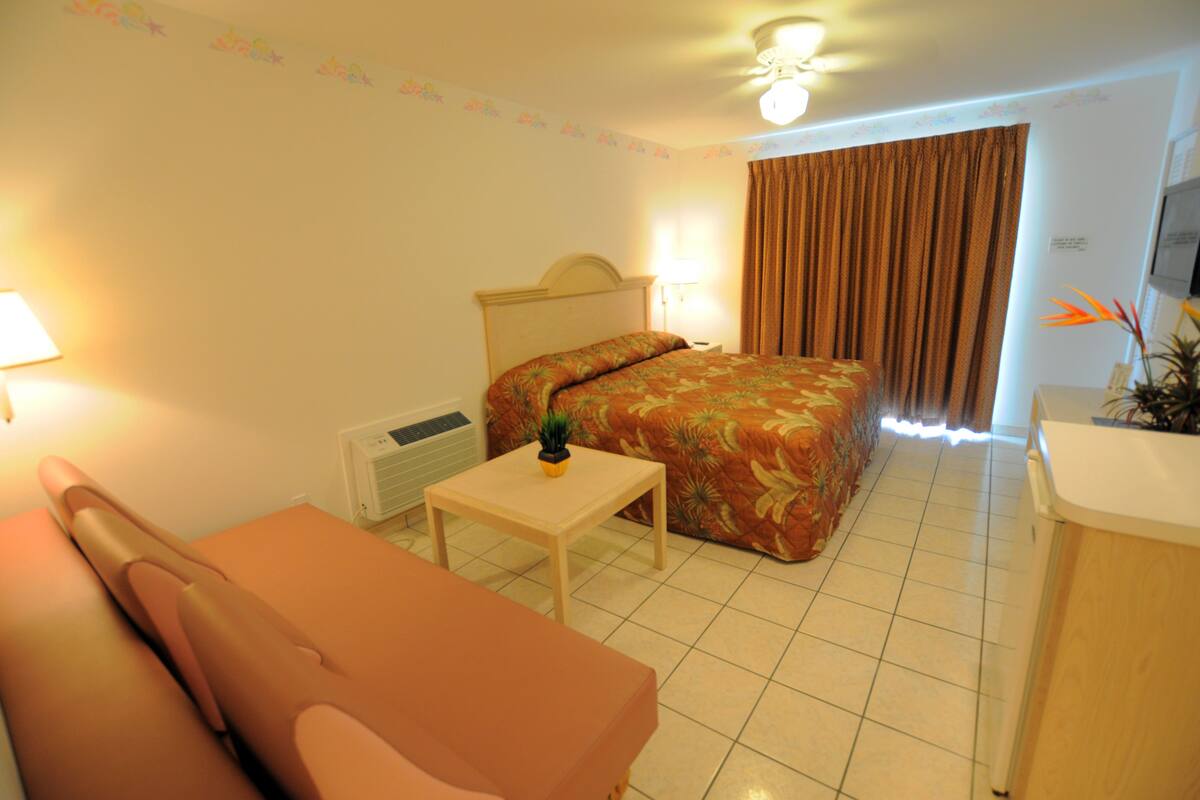 A hotel room with a bed, a small table with a plant, a sofa, and a desk with a lamp.