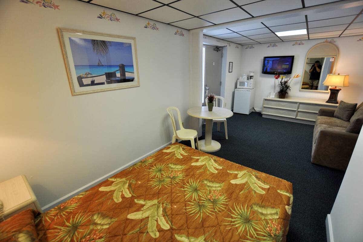 A hotel room with a bed, a small table, a chair, a sofa, a television, a coffee maker, and a mirror.