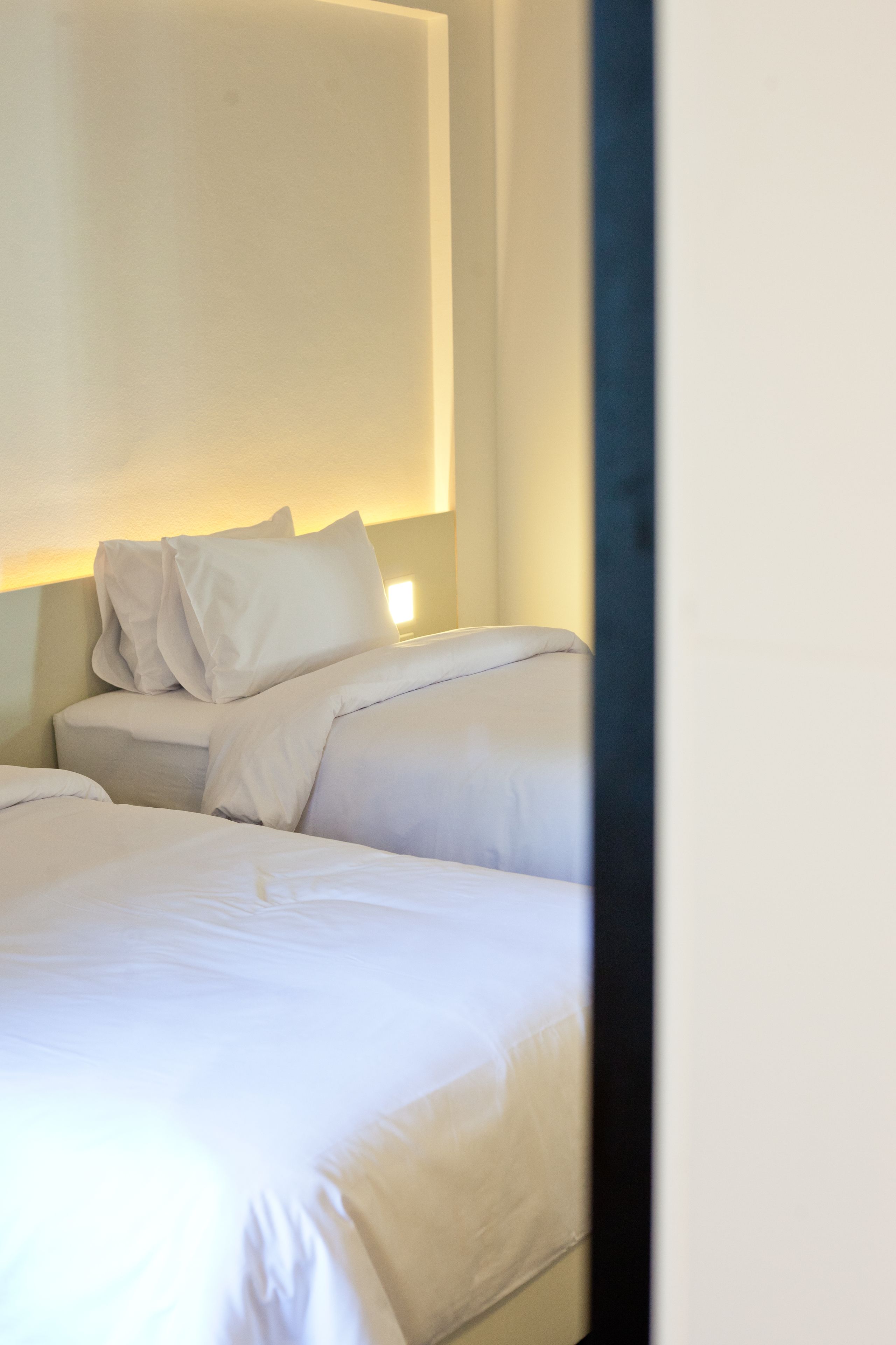 Un lit bien fait, avec du linge de lit blanc et des oreillers, une table de chevet avec une lampe et un mur sobre.