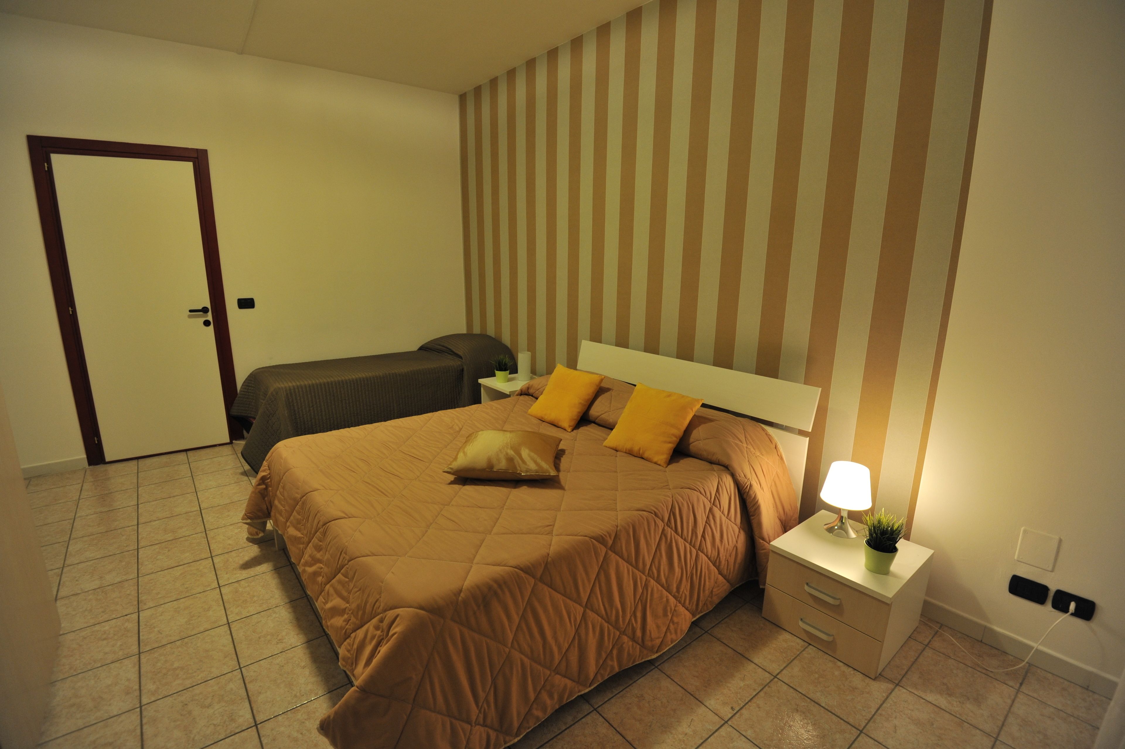 A bedroom with a large bed, a bedside table with a lamp, and a striped wall.