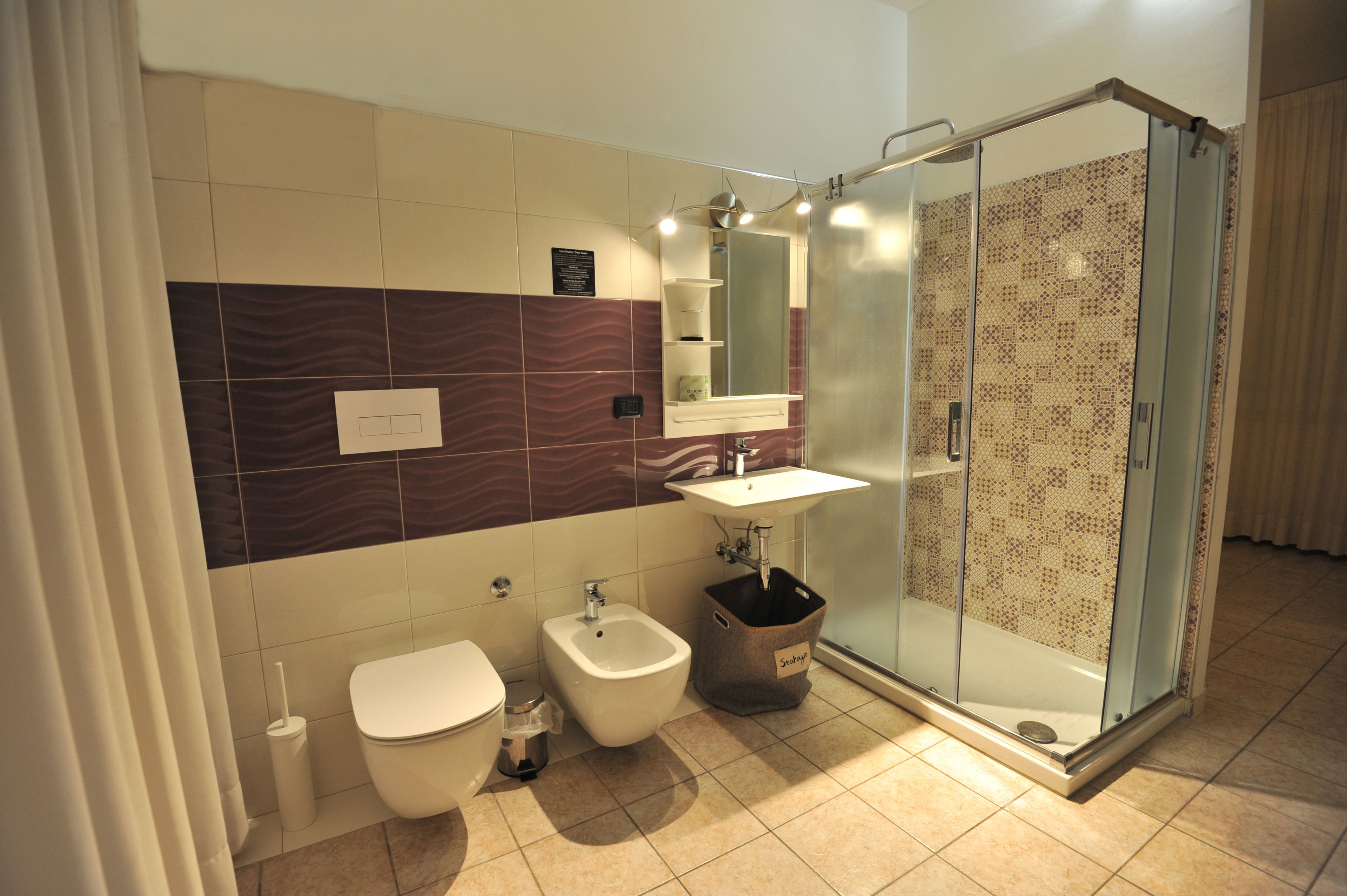 A modern bathroom with a bidet, toilet, sink, and glass-enclosed shower.