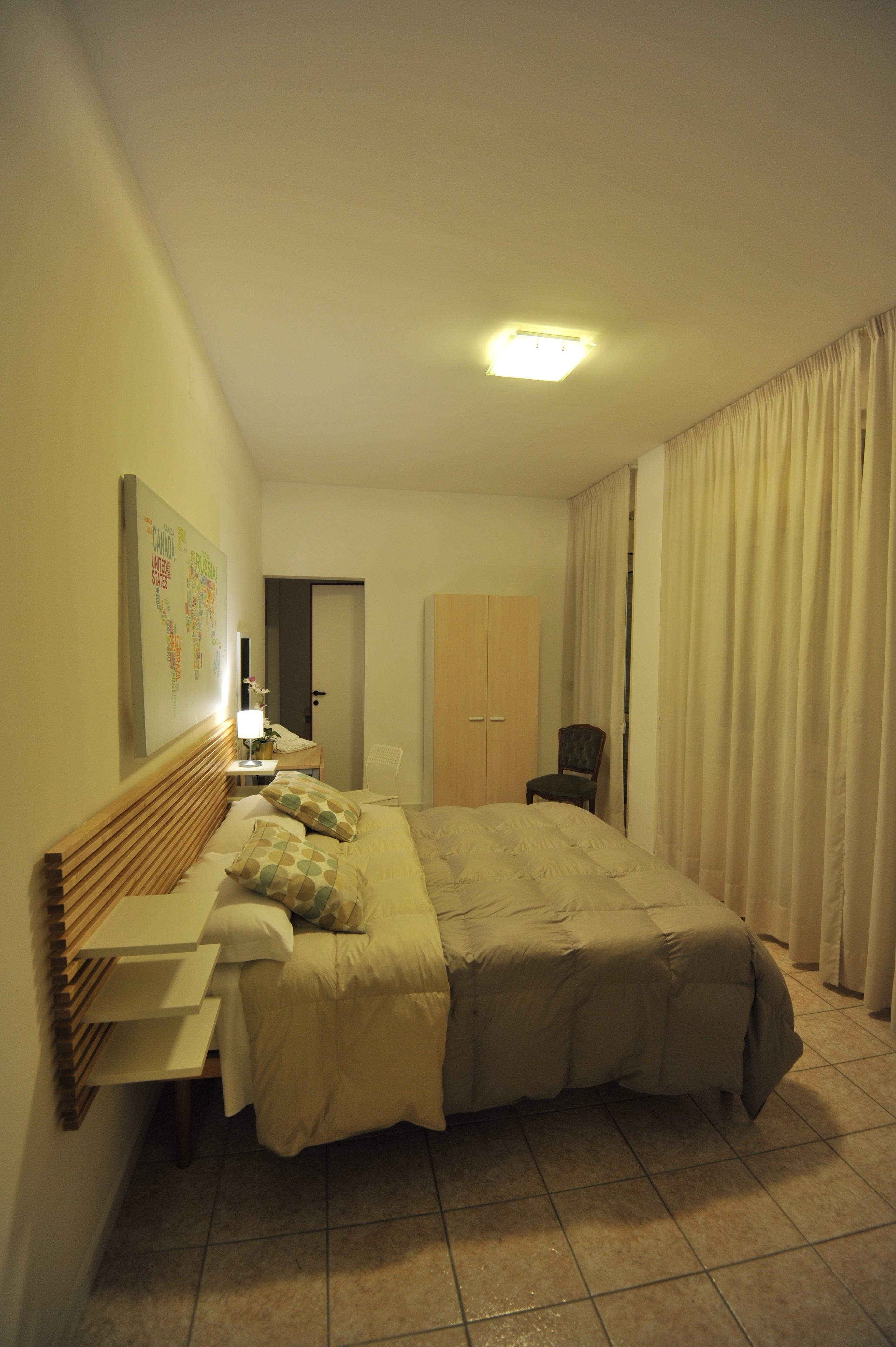 A hotel room with a bed, a chair, a wardrobe, and a door.