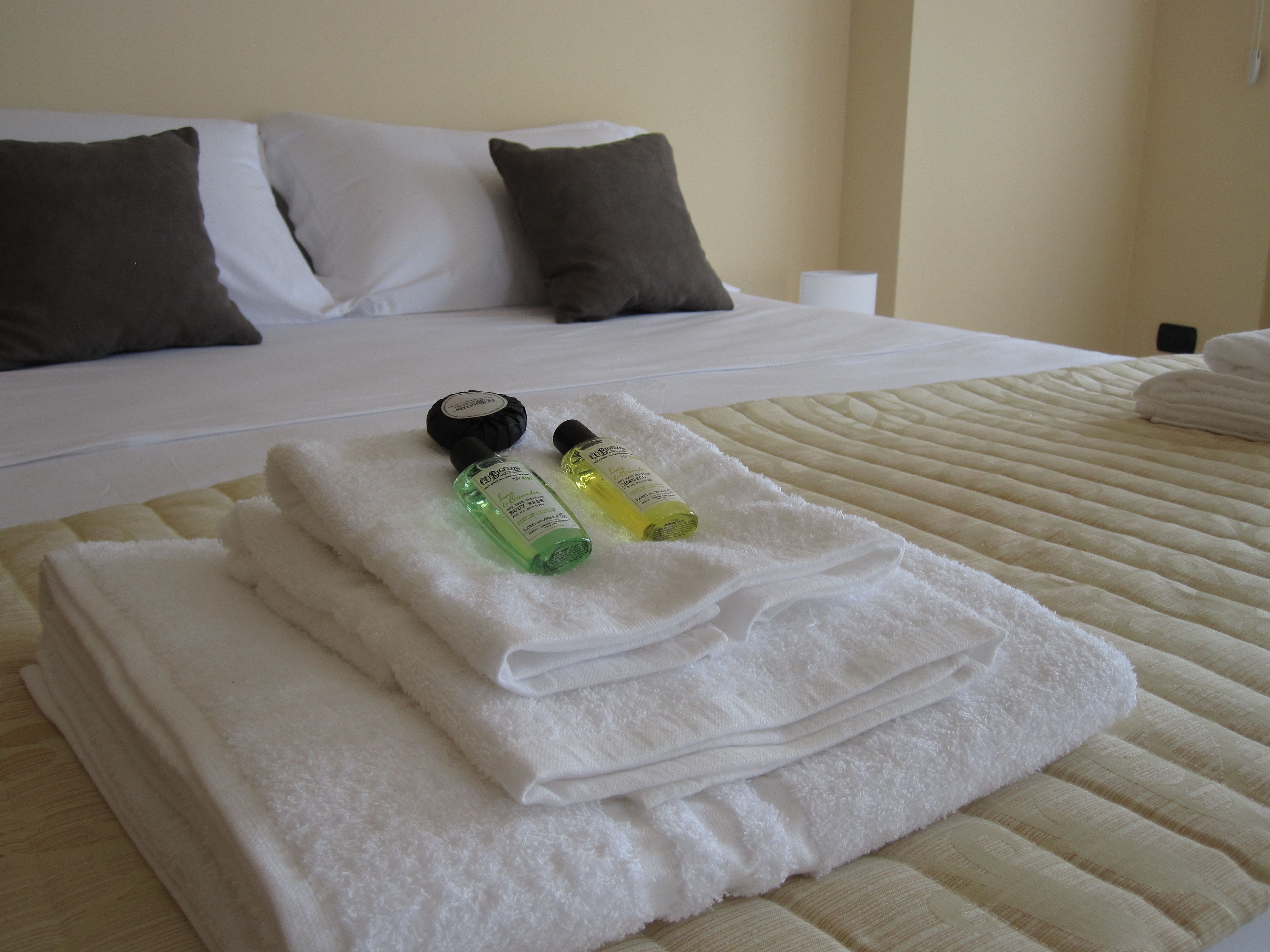 A neatly made bed with white and gray pillows, a folded white towel, and two bottles of body wash on a white towel.