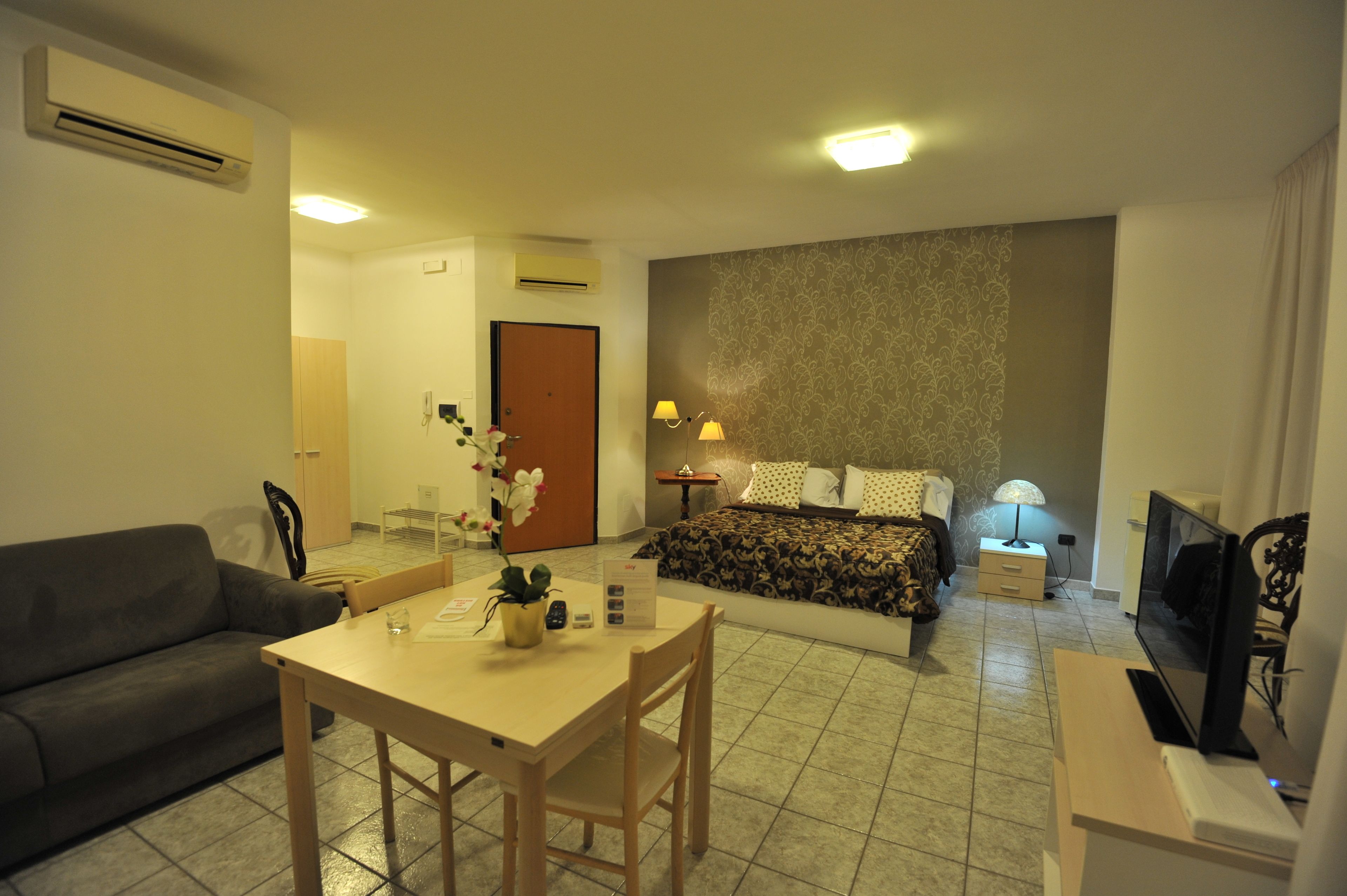 A hotel room with a bed, a TV, a desk with a chair, a sofa, and a dining table.