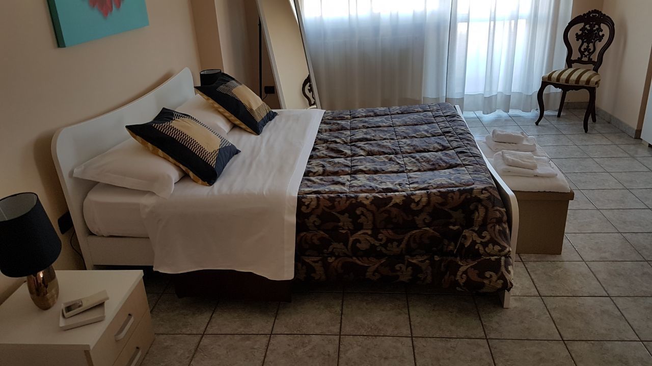 A bedroom with a double bed, a bedside table with a lamp, a chair, and a window with curtains.