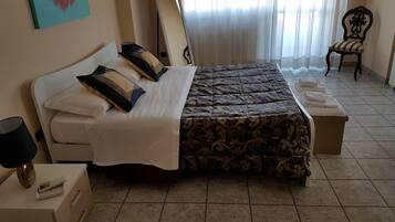 A bedroom with a double bed, a bedside table with a lamp, a chair, and a window with curtains.