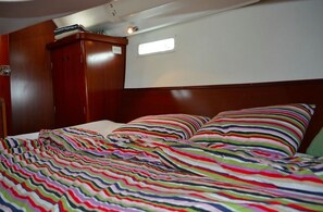 A bedroom with a wooden headboard, a bed with striped bedding, a wardrobe, and a small window.