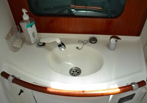A white sink with a wooden handle, a soap dispenser, and a glass container.