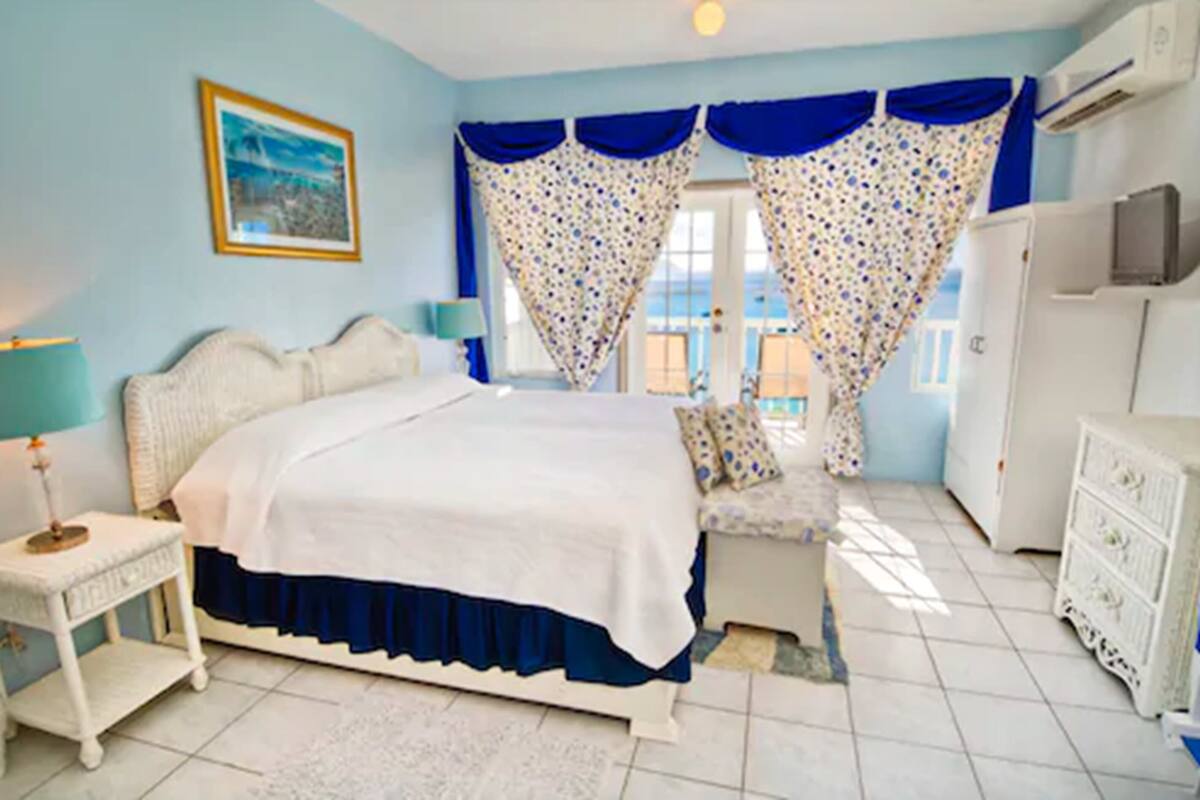 Un dormitorio con cama, mesitas de noche, cortinas, cómoda y televisor.