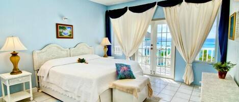 A bedroom with a bed, bedside tables, a bench, curtains, and a view of the outdoors.