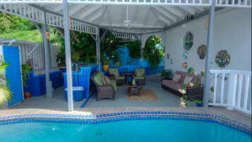 A covered outdoor pool area with seating and potted plants.