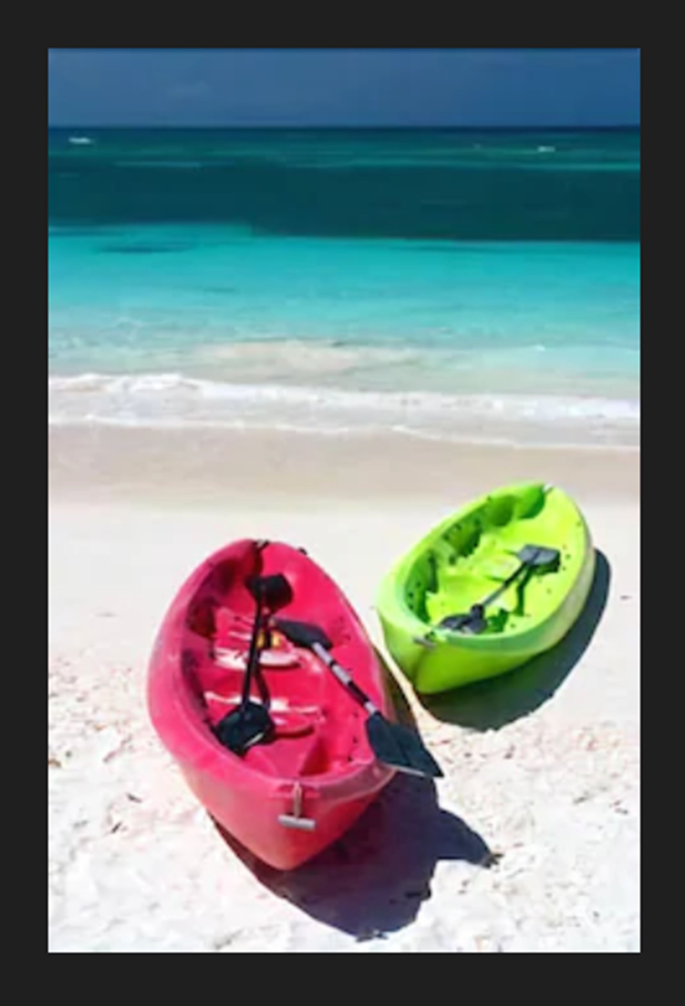 Dos kayaks sobre una playa arenosa, con un océano azul y transparente al fondo.