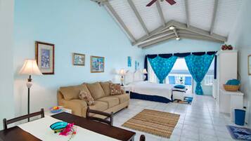 A room with a bed, a sofa, a dining table, and a ceiling fan.