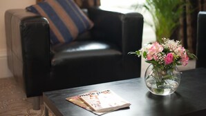A living room with a black leather sofa, a striped pillow, a glass vase with pink flowers, and a magazine on a wooden table. - Windsor Street Apartments (Edinburgh)