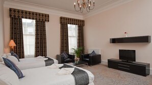 A hotel room with two beds, a TV, a sofa, and a coffee table. - Windsor Street Apartments (Edinburgh)