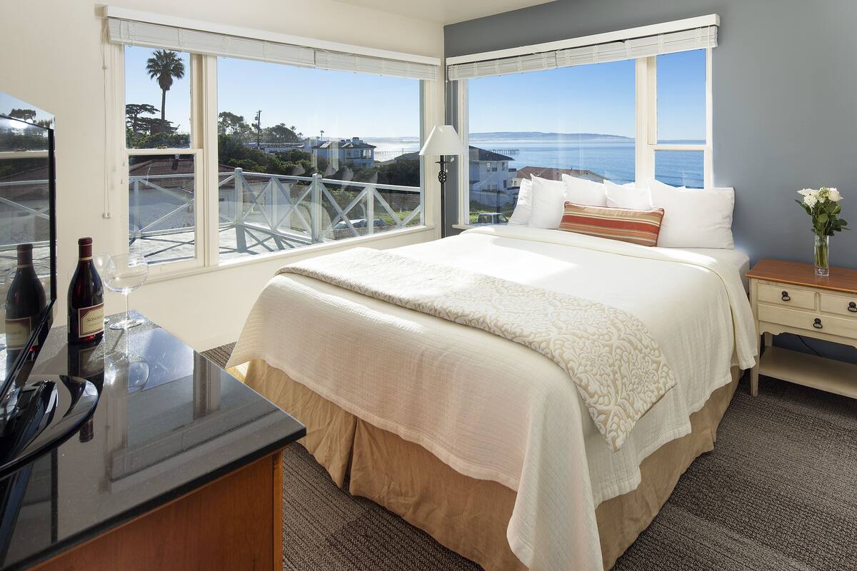 A bedroom with a bed, bedside table, lamp, and a view of the ocean.