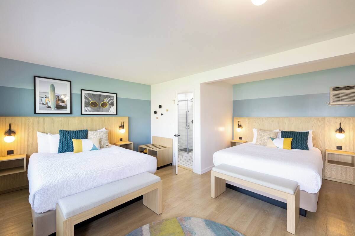 A modern hotel room with two beds, a shower area, and a small seating space.