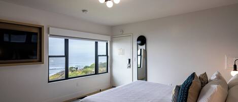 A bedroom with a large window, a bed with pillows, a ceiling light fixture, and a door.