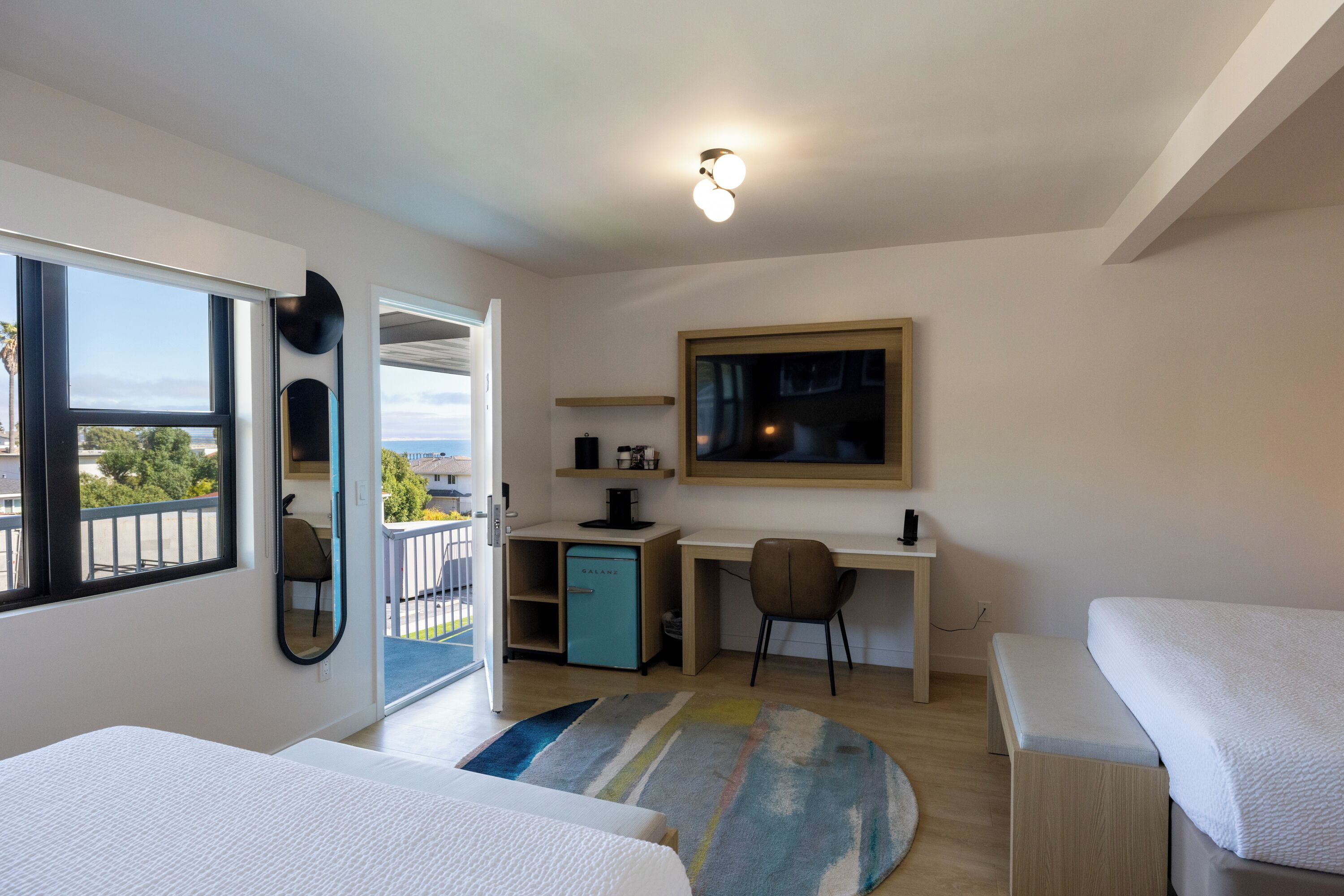 Un dormitorio moderno con cama, escritorio y silla. Hay un balcón con vistas al exterior.
