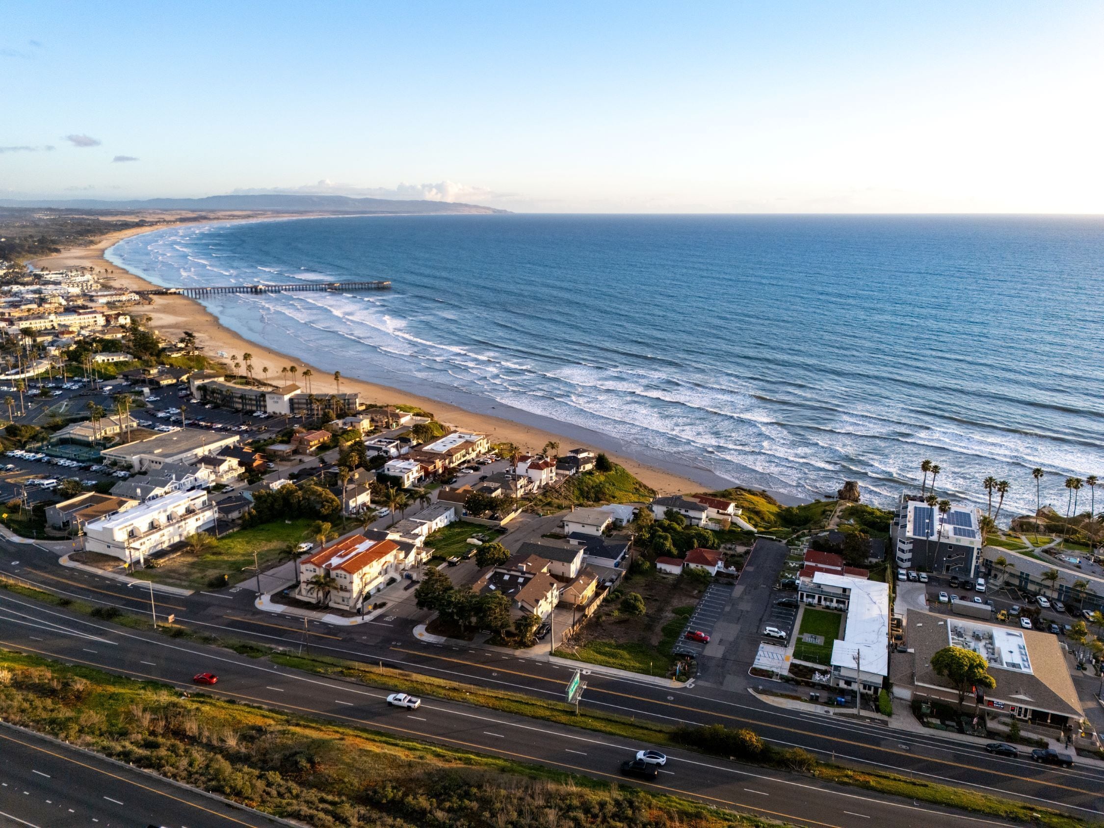 A coastal town with a beach, a pier, and a road with cars.