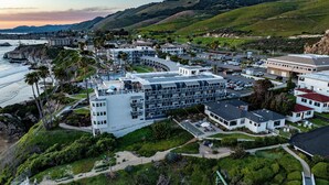 Ein Küstenhotel mit mehreren Gebäuden, darunter ein großes Hotel mit Schwimmbad und ein kleineres Gebäude mit rotem Dach.