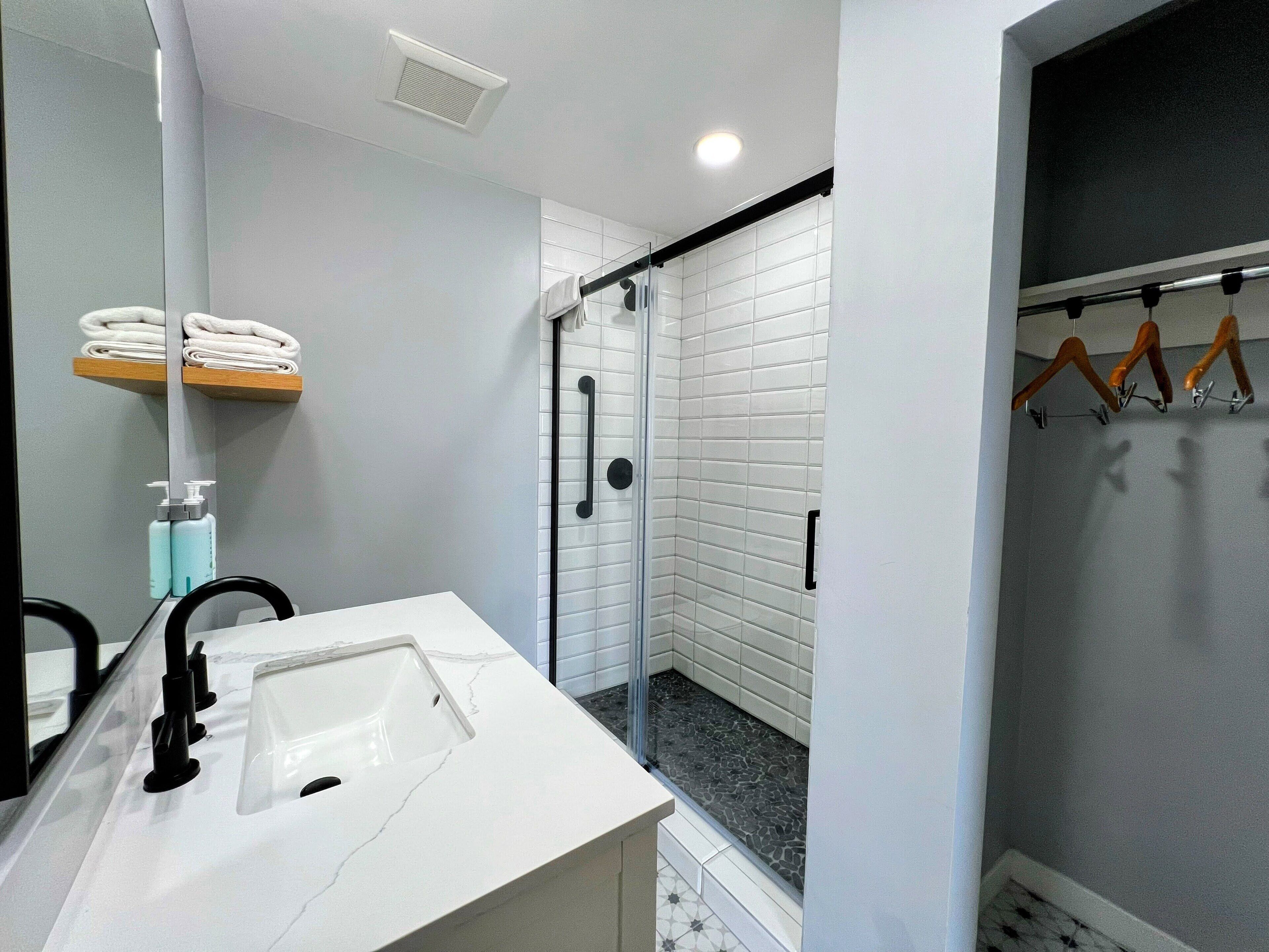 A modern bathroom with a white sink, a glass shower enclosure, and a towel rack with folded towels.