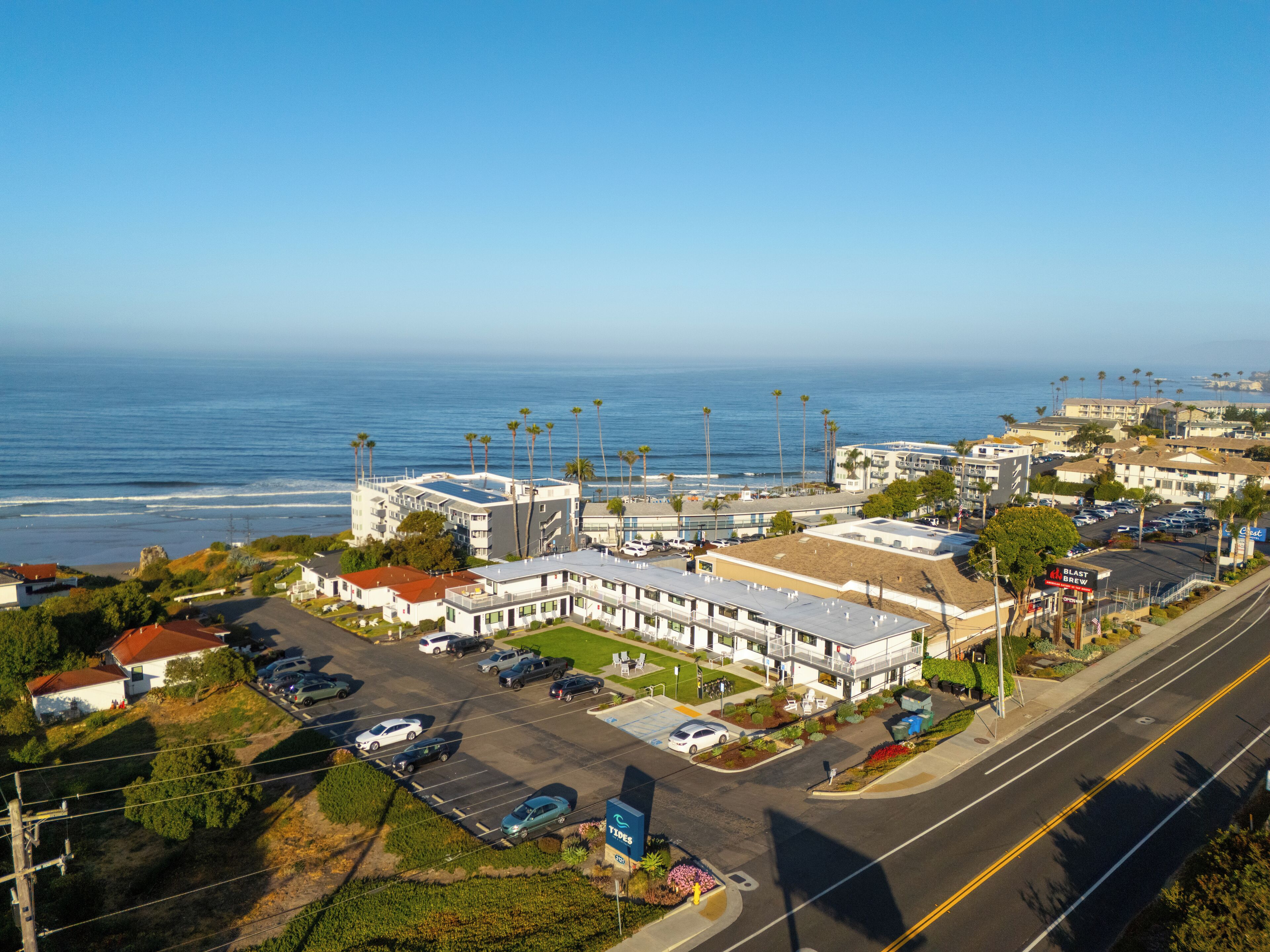 A coastal hotel with a parking lot, a view of the ocean, and a sign for 'BLAST BREW'.